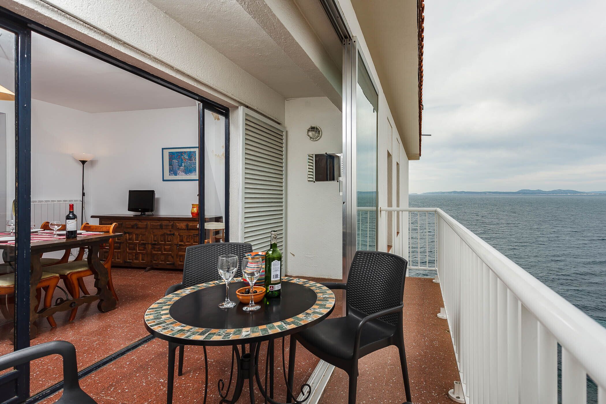 A balcony with a table set for dining, a chair, and a view of the sea.