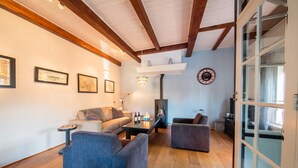 A cozy living room with a sofa, armchairs, a coffee table, and a fireplace. There are framed pictures on the wall and a clock.