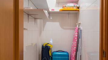 A small bathroom with a shower, a towel rack, and a shelf with toiletries.