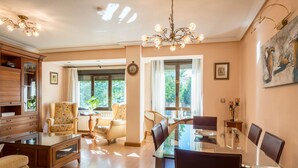 A spacious living room with a glass dining table, comfortable seating, and a chandelier.