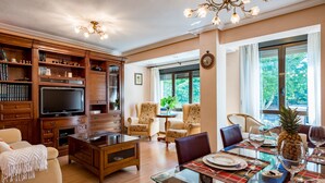 A spacious living room with a large flat-screen TV, wooden entertainment center, comfortable seating, and a dining area with a glass table.