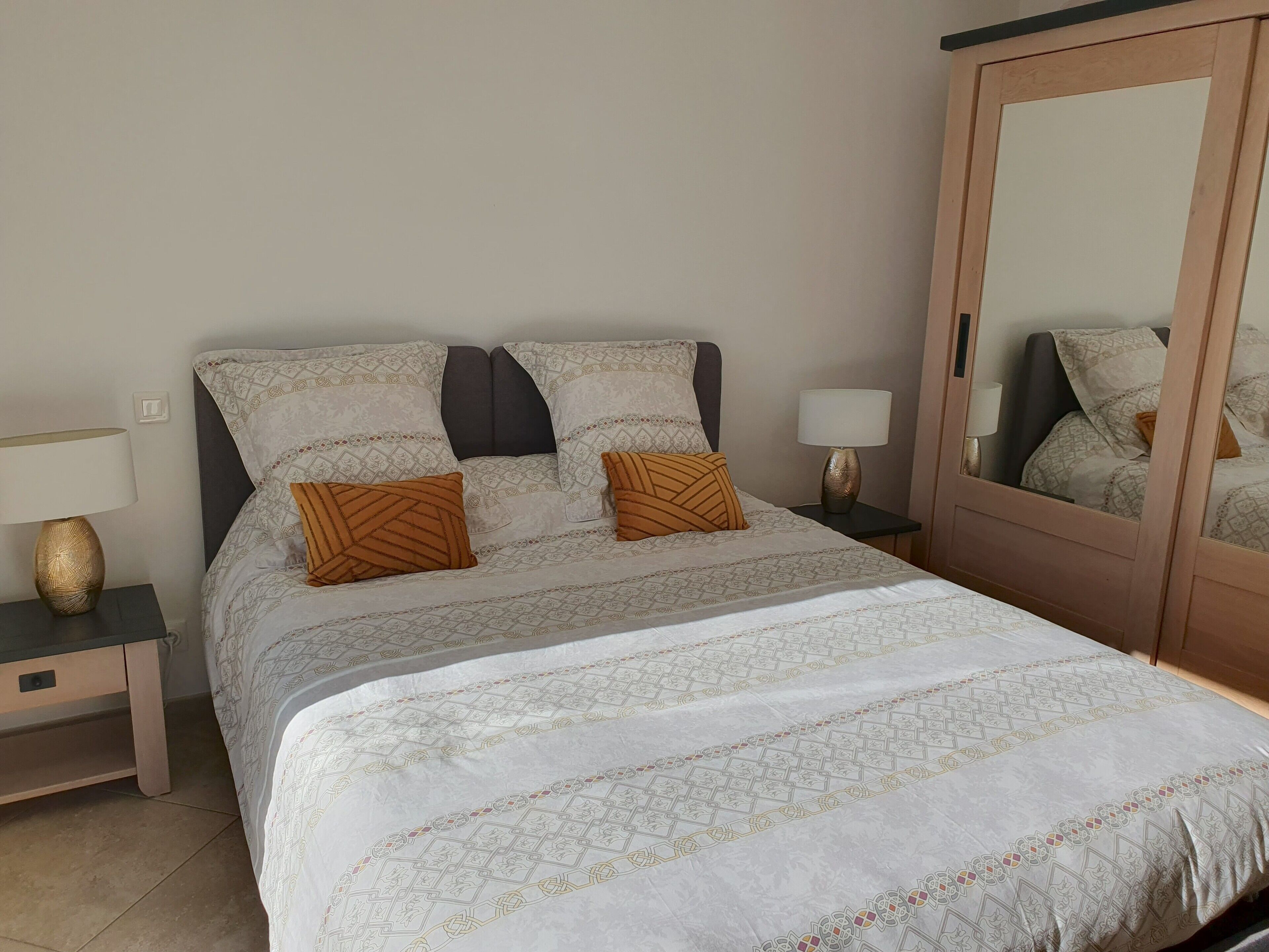 A neatly made bed with patterned bedding, two bedside lamps, a nightstand, and a mirror.