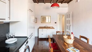 A modern kitchen with white cabinets, a wooden dining table, and a red pendant light.