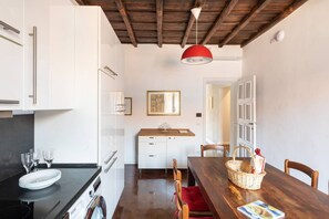 A modern kitchen with white cabinets, a wooden dining table, and a red pendant light. - Residenza Torre Vecchiarelli - apt 4 (Roma)