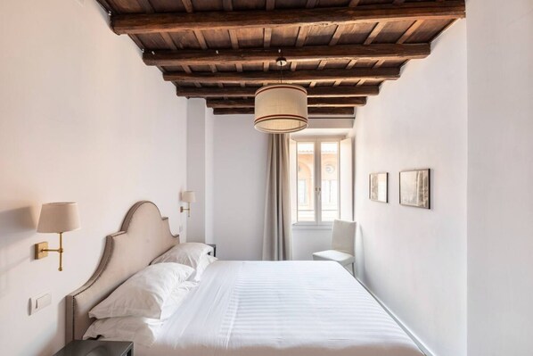 A hotel room with a wooden ceiling, a bed with white linens, a wall-mounted lamp, and a window with curtains. - Residenza Torre Vecchiarelli - apt 4 (Roma)