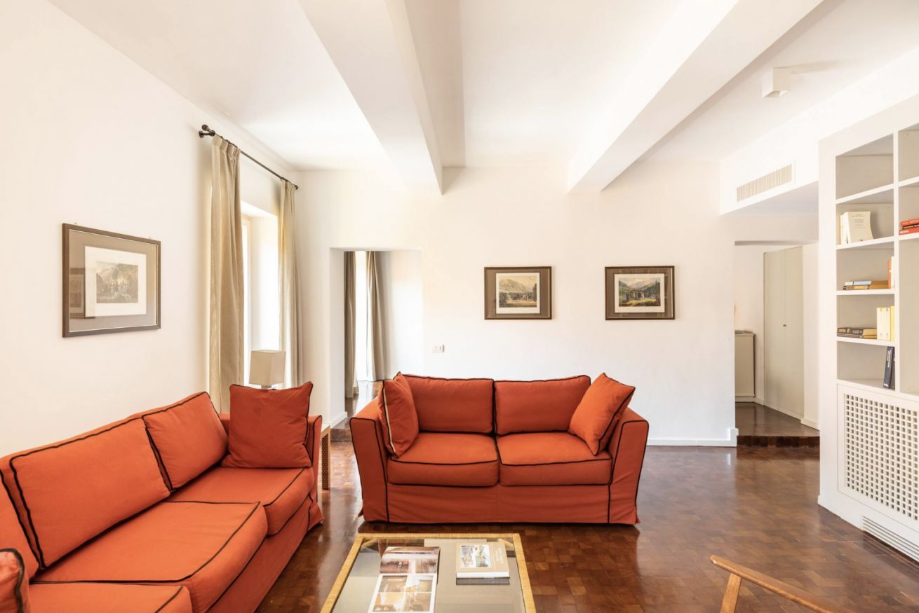 A spacious living room with two orange sofas, a coffee table, and framed pictures on the walls.