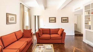 A spacious living room with two orange sofas, a coffee table, and framed pictures on the walls.
