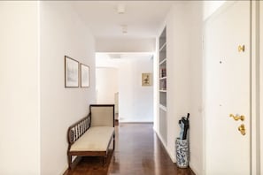 A hallway with a bench, framed pictures on the wall, a white door with a gold handle, and a blue vase with a pen holder. - Residenza Torre Vecchiarelli - apt 4 (Roma)