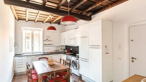 A kitchen with white cabinets, a wooden table with red chairs, and a washing machine. - Residenza Torre Vecchiarelli - apt 4 (Roma)
