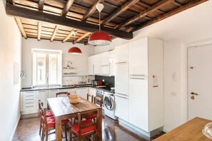 A kitchen with white cabinets, a wooden table with red chairs, and a washing machine. - Residenza Torre Vecchiarelli - apt 4 (Roma)