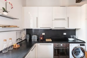 A modern kitchen with white cabinets, a black countertop, a built-in oven, a washing machine, and a small shelf with a potted plant. - Residenza Torre Vecchiarelli - apt 4 (Roma)