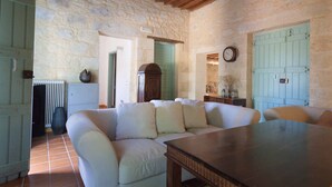 A rustic room with a stone wall, a wooden ceiling, a green door, a white sofa, and a wooden table. - Traditional Stone Villa with Sea Views, Private Pool and 10 mins from beach (Karefiliana)
