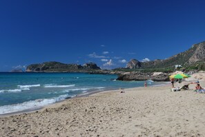 Una platja amb aigua turquesa cristal·lina, penya-segats rocosos i poques persones.