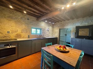 Une cuisine rustique avec des murs en pierre, un plafond en bois et une table à manger entourée de chaises.