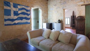 A cozy room with a stone wall, a white sofa, and a painting of waves. - Traditional Stone Villa with Sea Views, Private Pool and 10 mins from beach (Karefiliana)