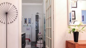 A bathroom with a shower, a toilet, a sink, and a mirror. There are towels stacked on a rack and a vase with flowers on a table. - 3 Bedroom Air Conditioned Apartment In The Heart Of Old Town Nice (Nice)