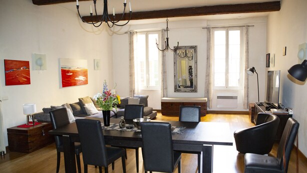 A dining area with a table set for four, surrounded by chairs, a chandelier, and a vase with flowers. - 3 Bedroom Air Conditioned Apartment In The Heart Of Old Town Nice (Nice)