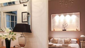 A hotel room with a bed, bedside table, lamp, vase with flowers, and a mirror. - 3 Bedroom Air Conditioned Apartment In The Heart Of Old Town Nice (Nice)