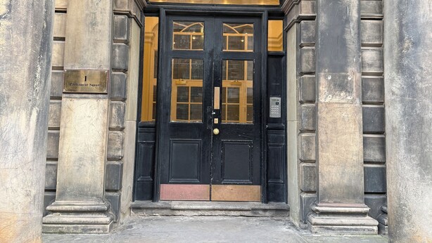 Una porta doppia nera con pannelli di vetro, affiancata da colonne in pietra, che dà accesso a un ingresso.