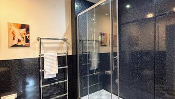Un baño con piso a cuadros blanco y negro, cabina de ducha de vidrio, toallero y un inodoro.