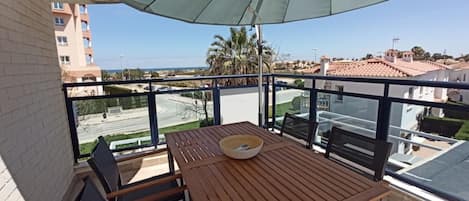 Un balcón con mesa y sillas de madera, un cuenco y vista a una calle y edificios.