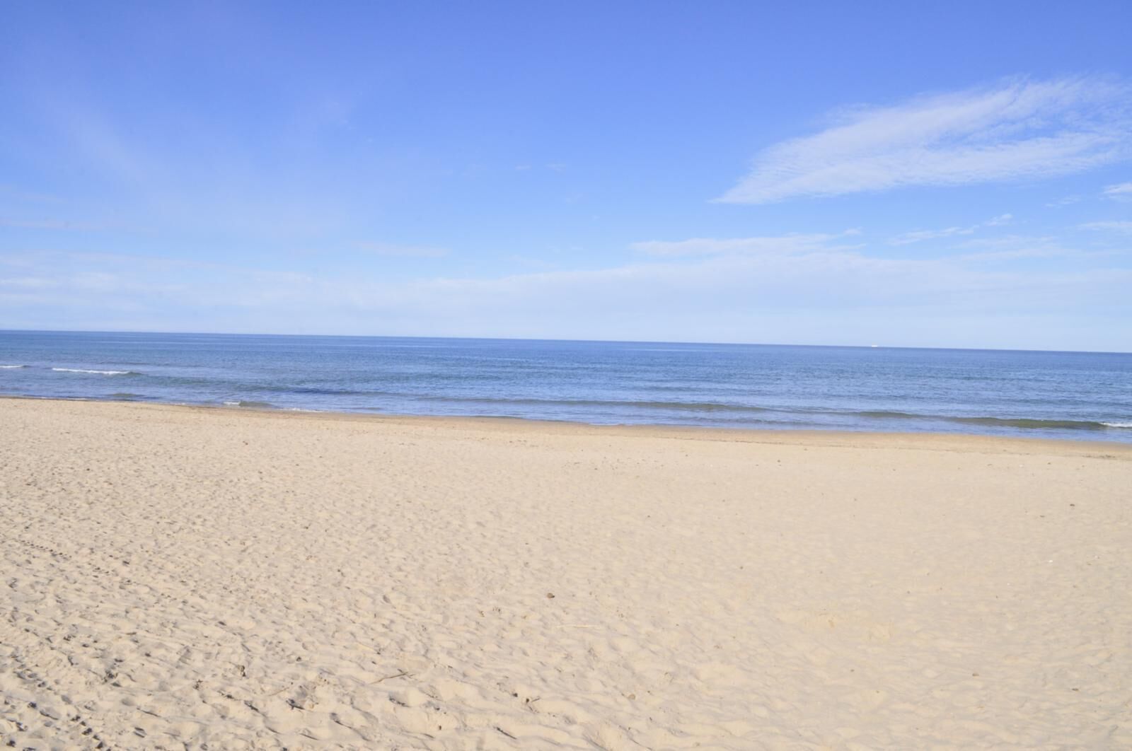 Una spiaggia ampia e sabbiosa, con onde calme e cielo sereno.