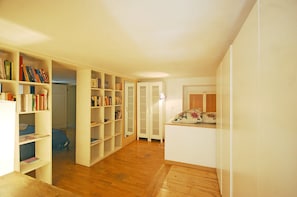 A spacious room with wooden flooring, white walls, and a large bookshelf filled with books.