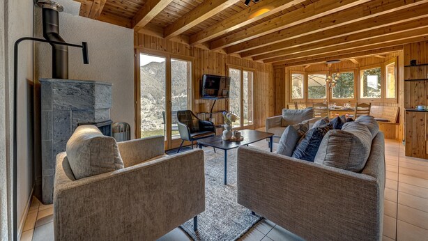 Un amplio salón con chimenea de piedra, vigas de madera en el techo y grandes ventanales con vistas a las montañas.
