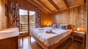 Un dormitorio de cabaña de madera con una cama grande, un escritorio y vistas a las montañas.