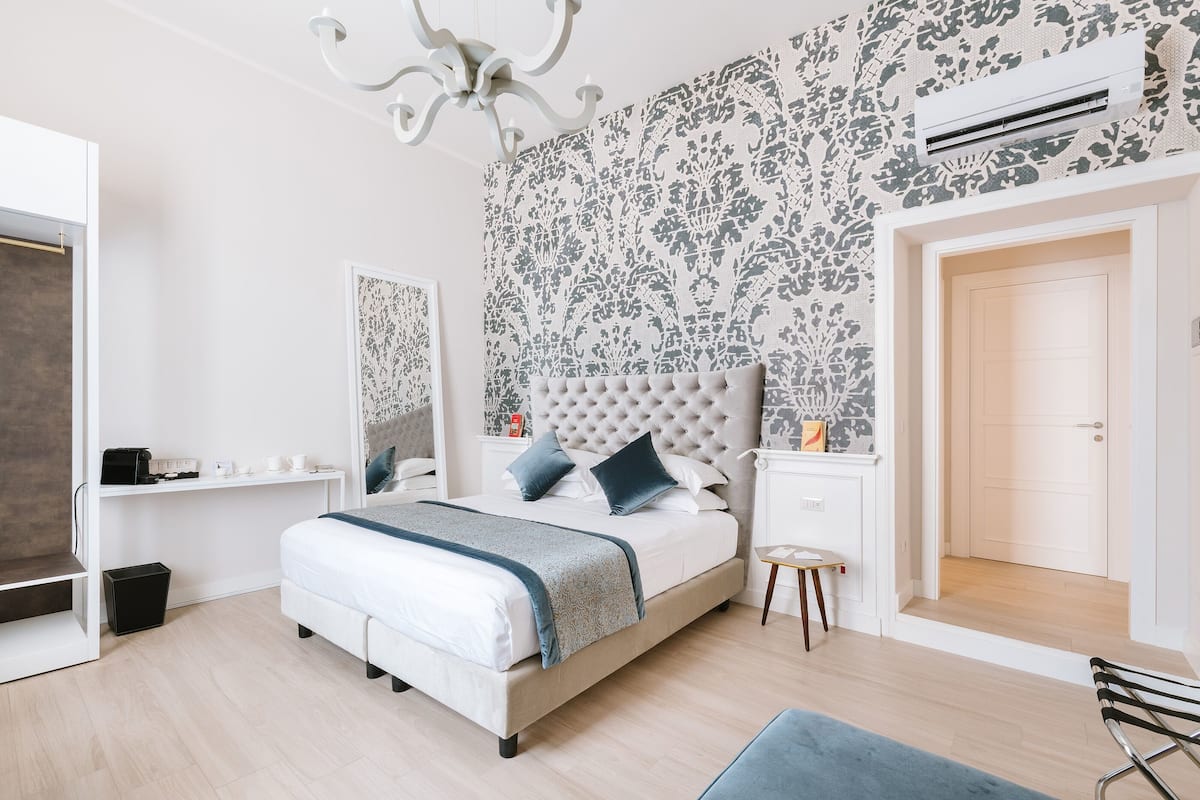 Une chambre à coucher avec un lit, des tables de chevet, une chaise, un petit tabouret et une porte.