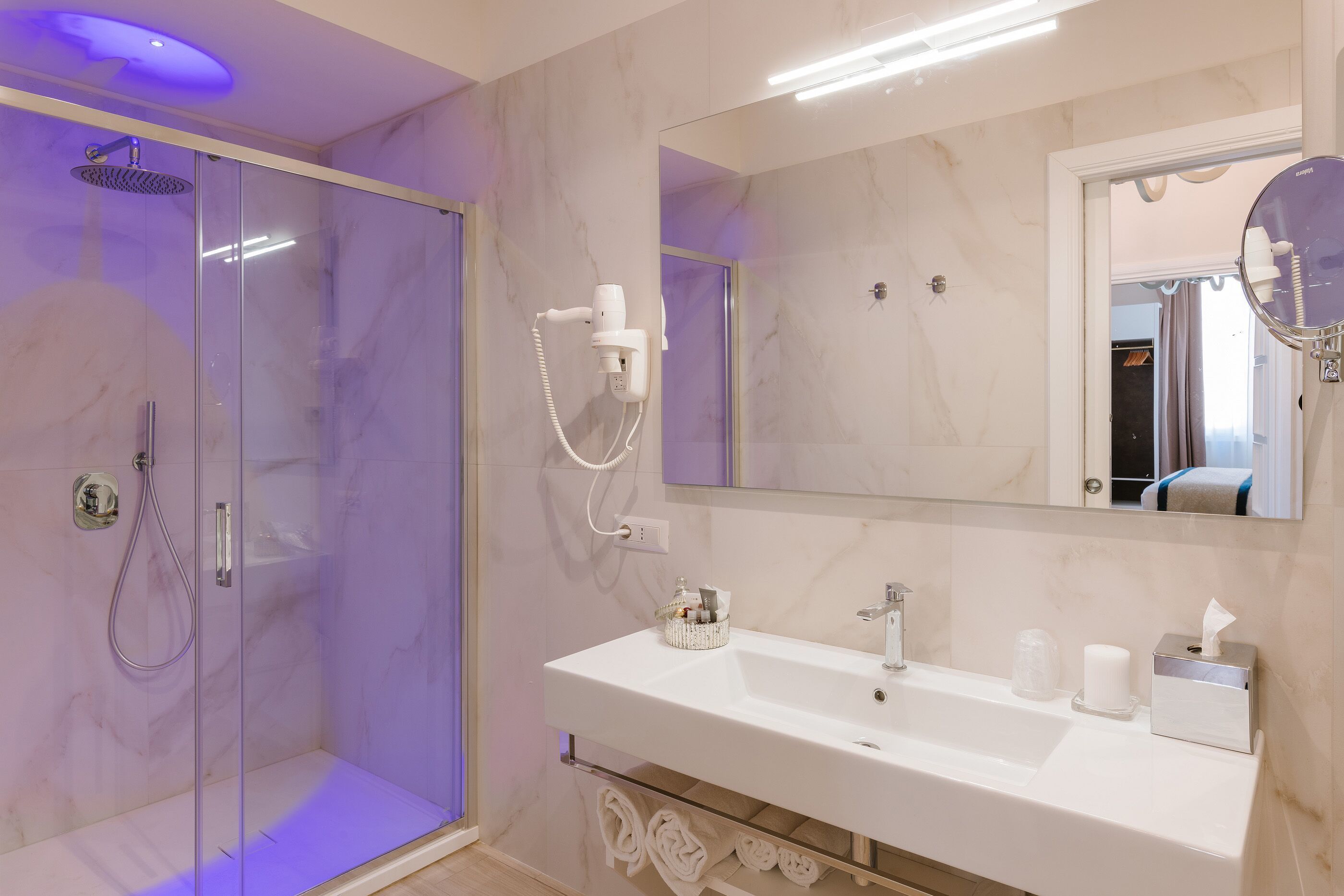 A modern bathroom with a glass-enclosed shower, a white sink with a mirror above, and a towel rack below.