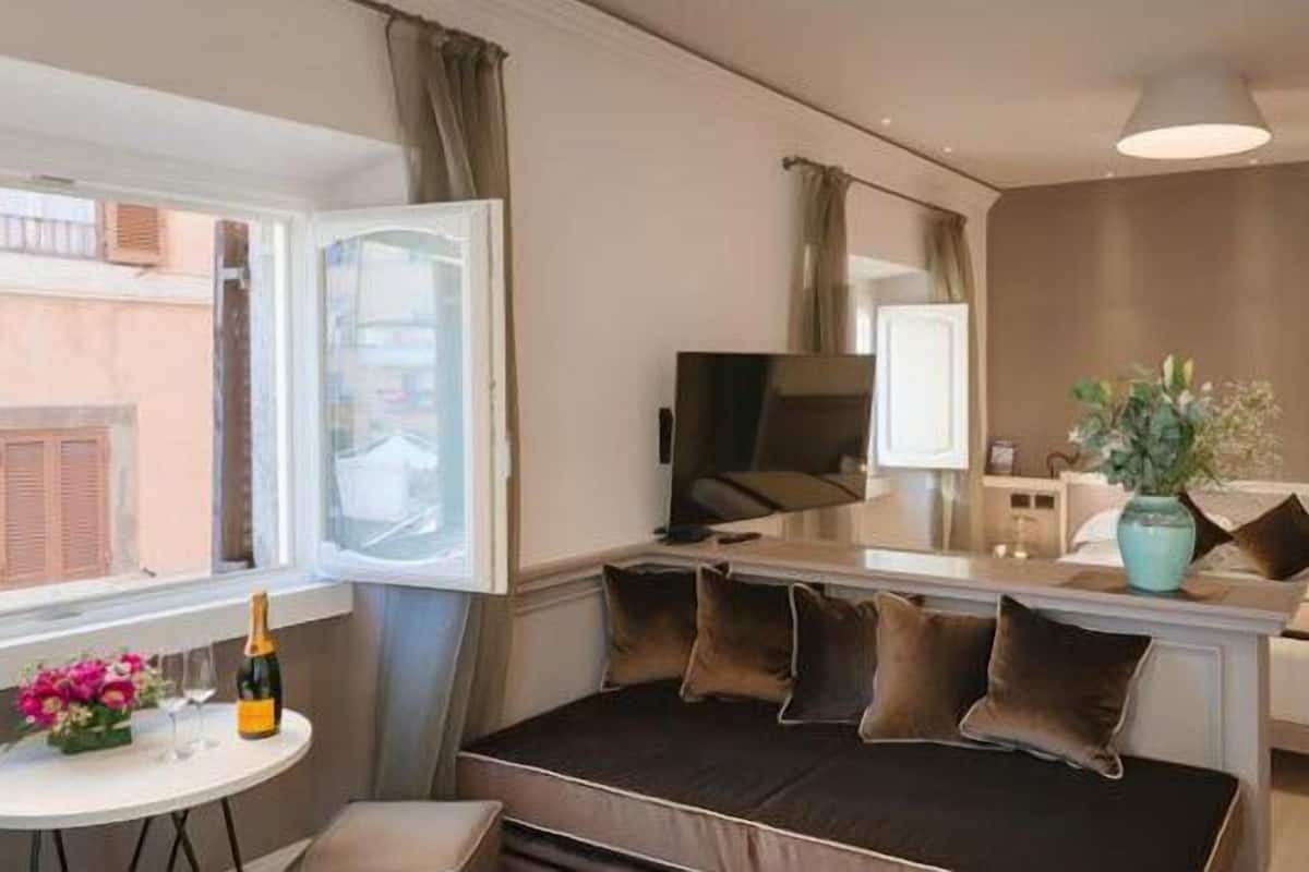 Un espace de vie compact comprenant un canapé, une petite table avec une bouteille et des fleurs, un téléviseur et une plante.