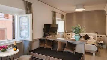 A compact living space with a sofa, a small table with a bottle and flowers, a TV, and a plant.