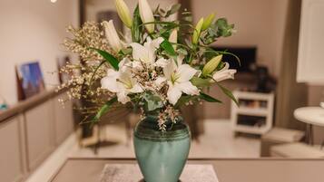 Un florero azul aguamarina con flores blancas y hojas verdes sobre una mesa en una habitación con una paleta de colores neutros y decoración moderna.