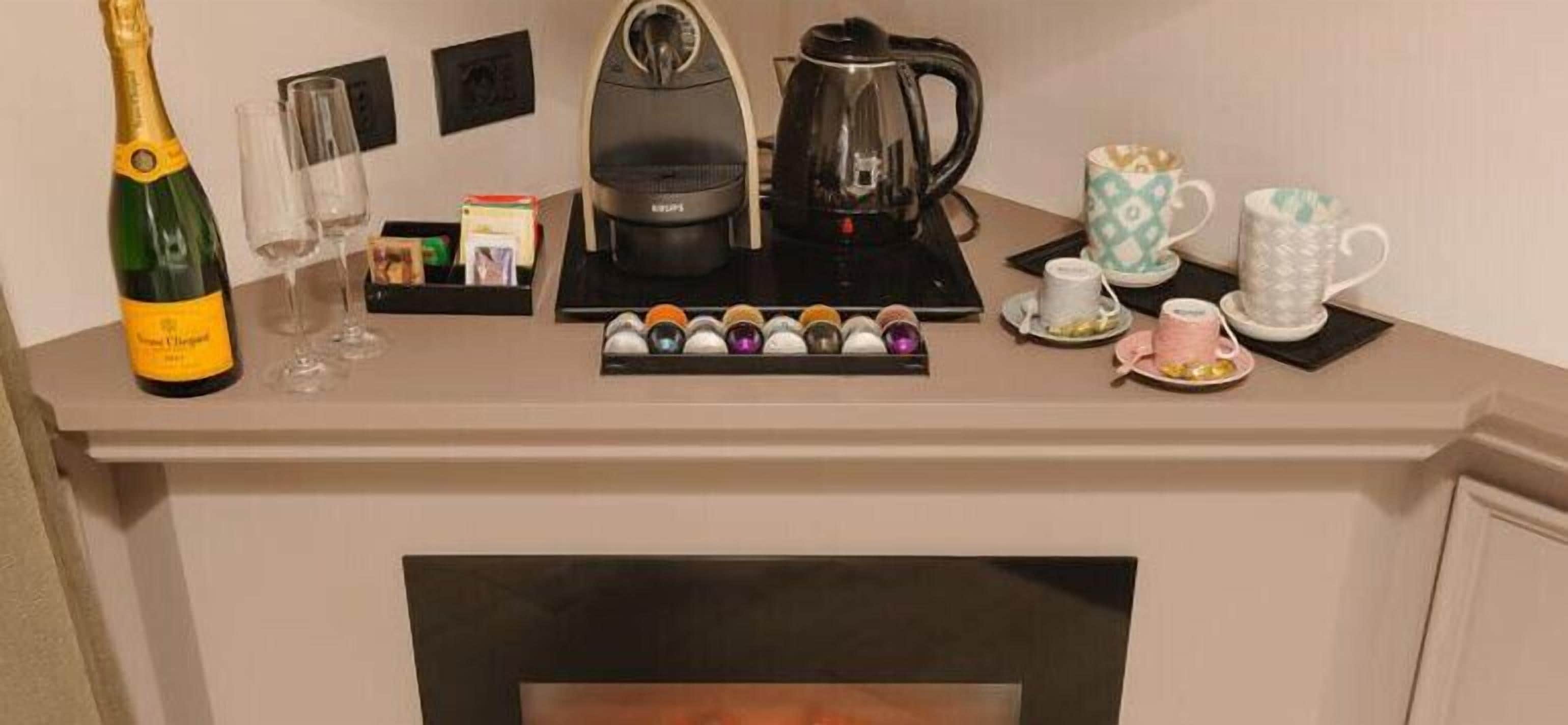 A coffee station with a coffee maker, tea cups, and a bottle of champagne on a counter.