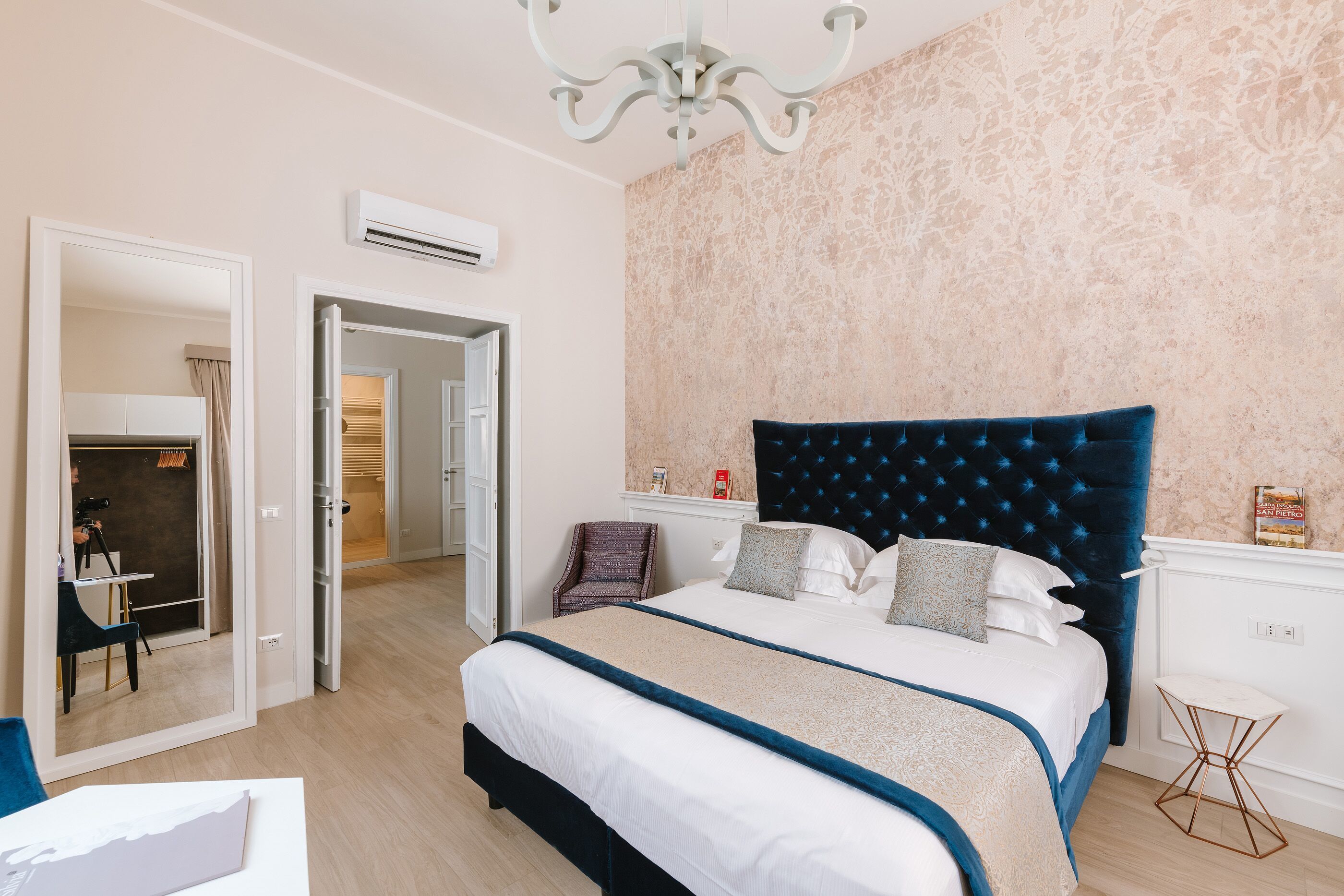 A bedroom with a large bed, a chair, a small table, and an air conditioning unit.