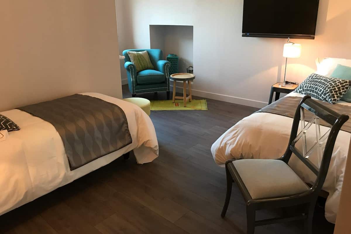 Une chambre d’hôtel avec deux lits, une chaise, une petite table, un téléviseur et une lampe.