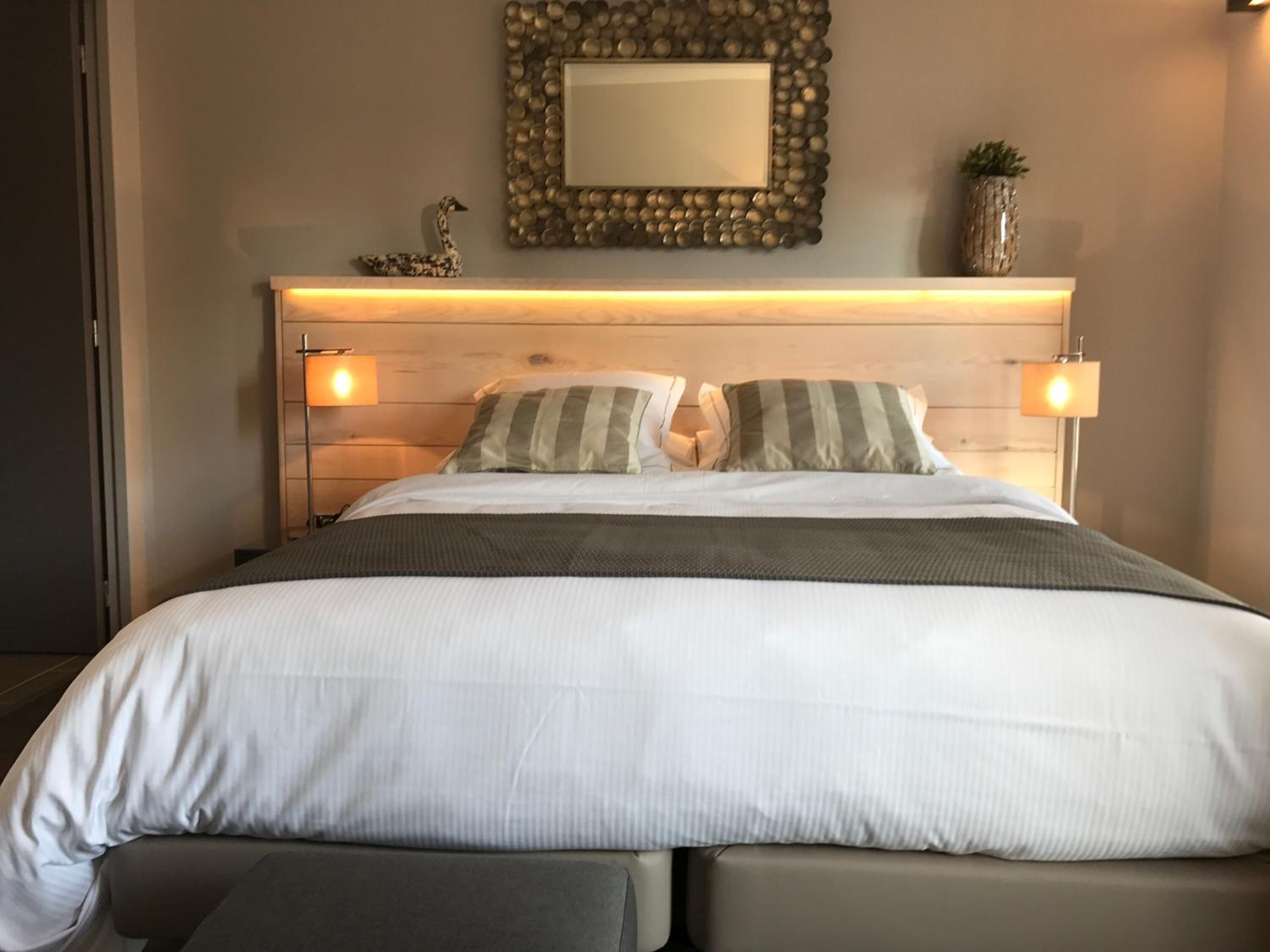 A neatly made bed with two pillows, a bedside table with a lamp, and a decorative mirror on the wall.