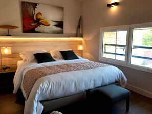 A bedroom with a large bed, two bedside lamps, a nightstand, a bench, a window with a view, and a painting on the wall. - Le Relais d'Aligre (Chateauneuf-en-Thymerais)