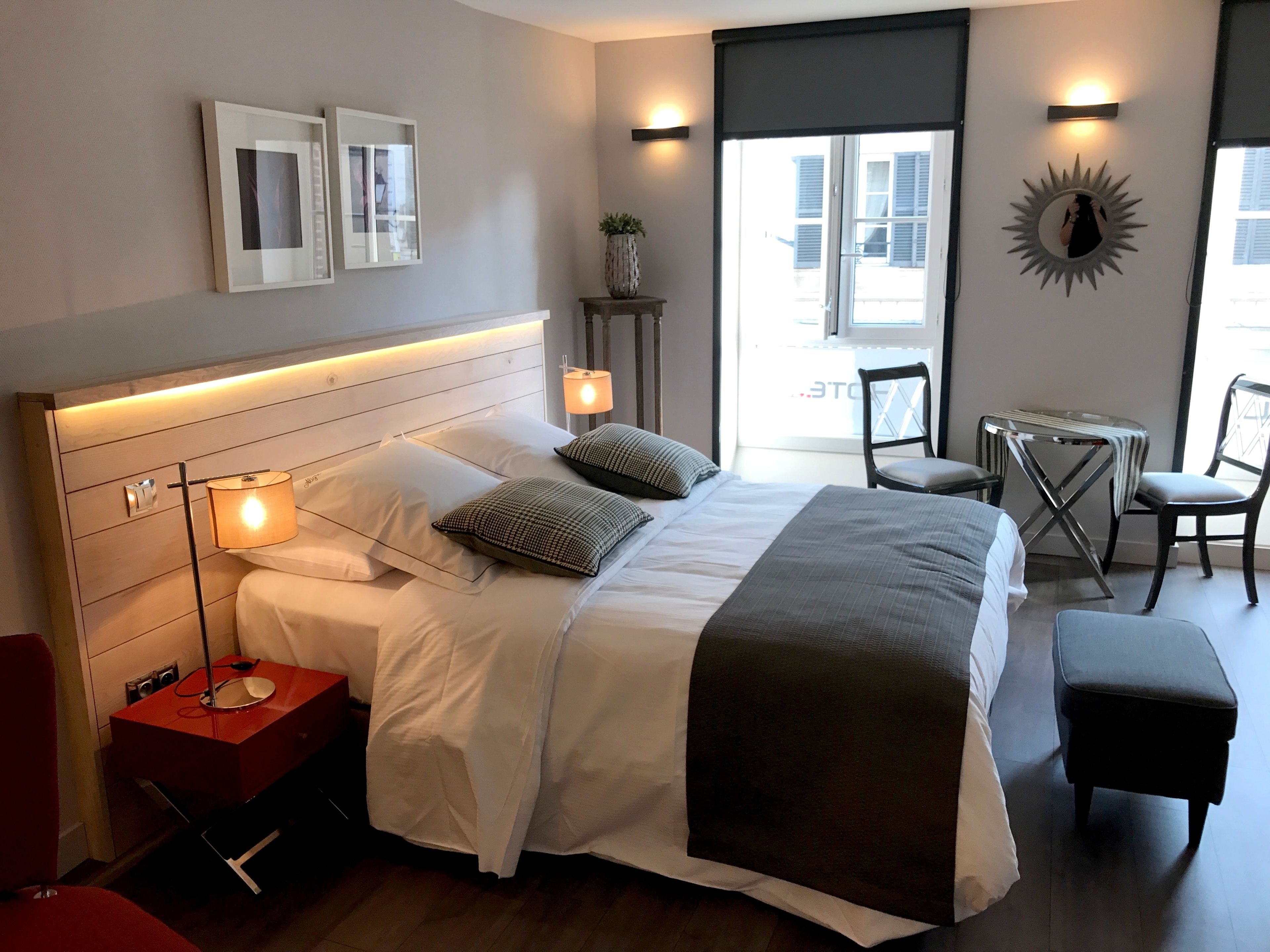 A modern hotel room with a large bed, bedside lamps, a small table with a chair, and a view of the outside.
