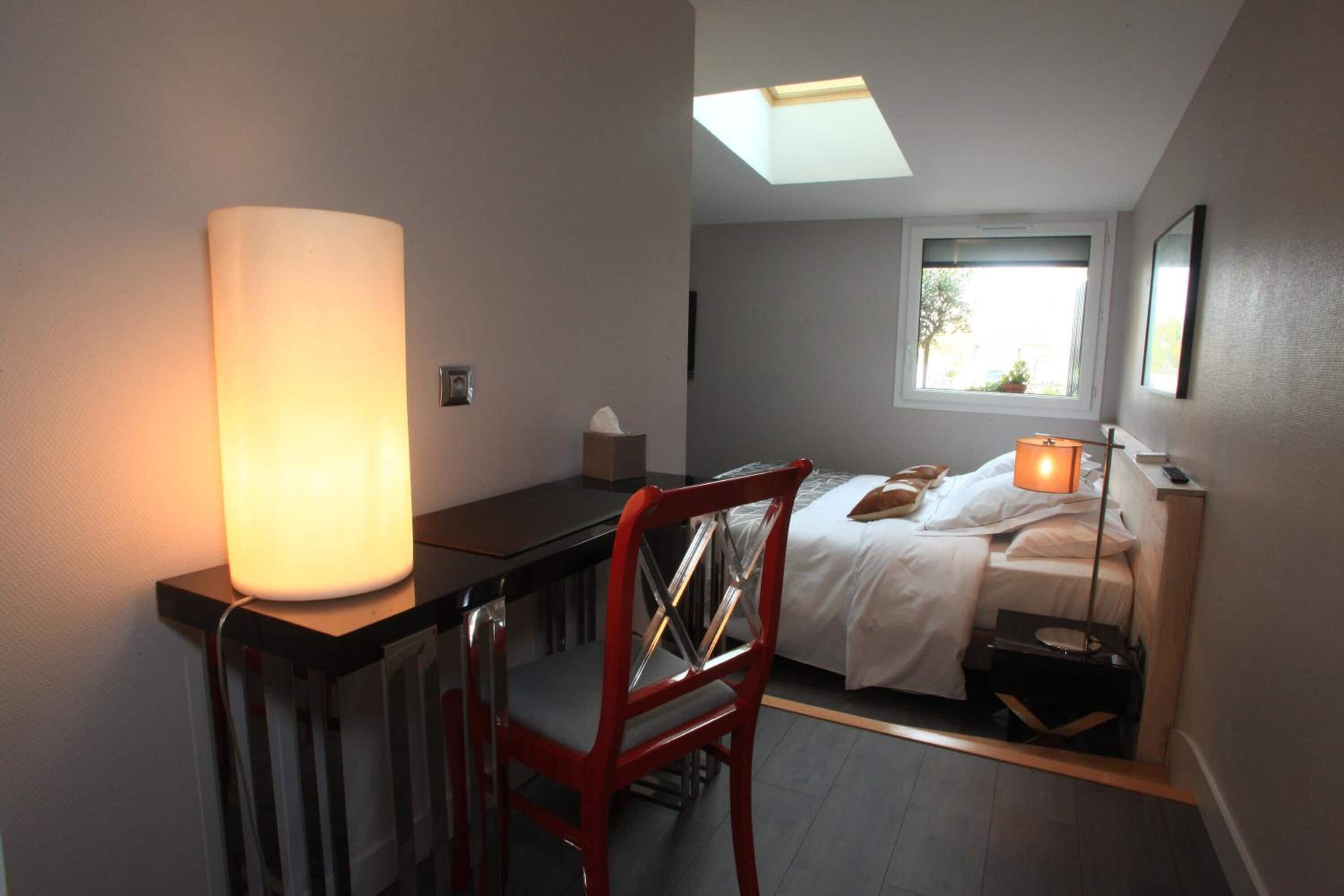 A compact hotel room with a desk, chair, bed, and skylight.