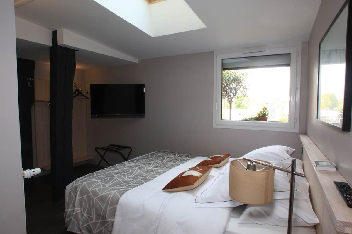 Une chambre d’hôtel avec un lit, un téléviseur fixé au mur, une fenêtre donnant sur l’extérieur et un bureau avec une lampe et une télécommande.