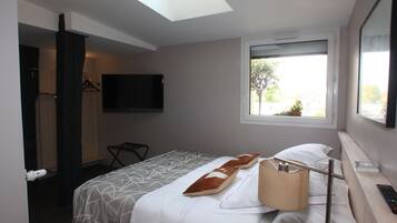 A hotel room with a bed, a TV mounted on the wall, a window with a view of the outside, and a desk with a lamp and remote control.