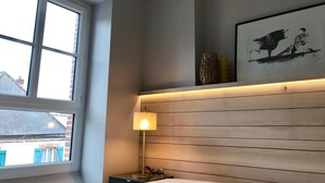 Una habitació amb un gran finestral, una làmpada de nit, un capçal de llit de fusta i una obra d'art emmarcada a la paret.