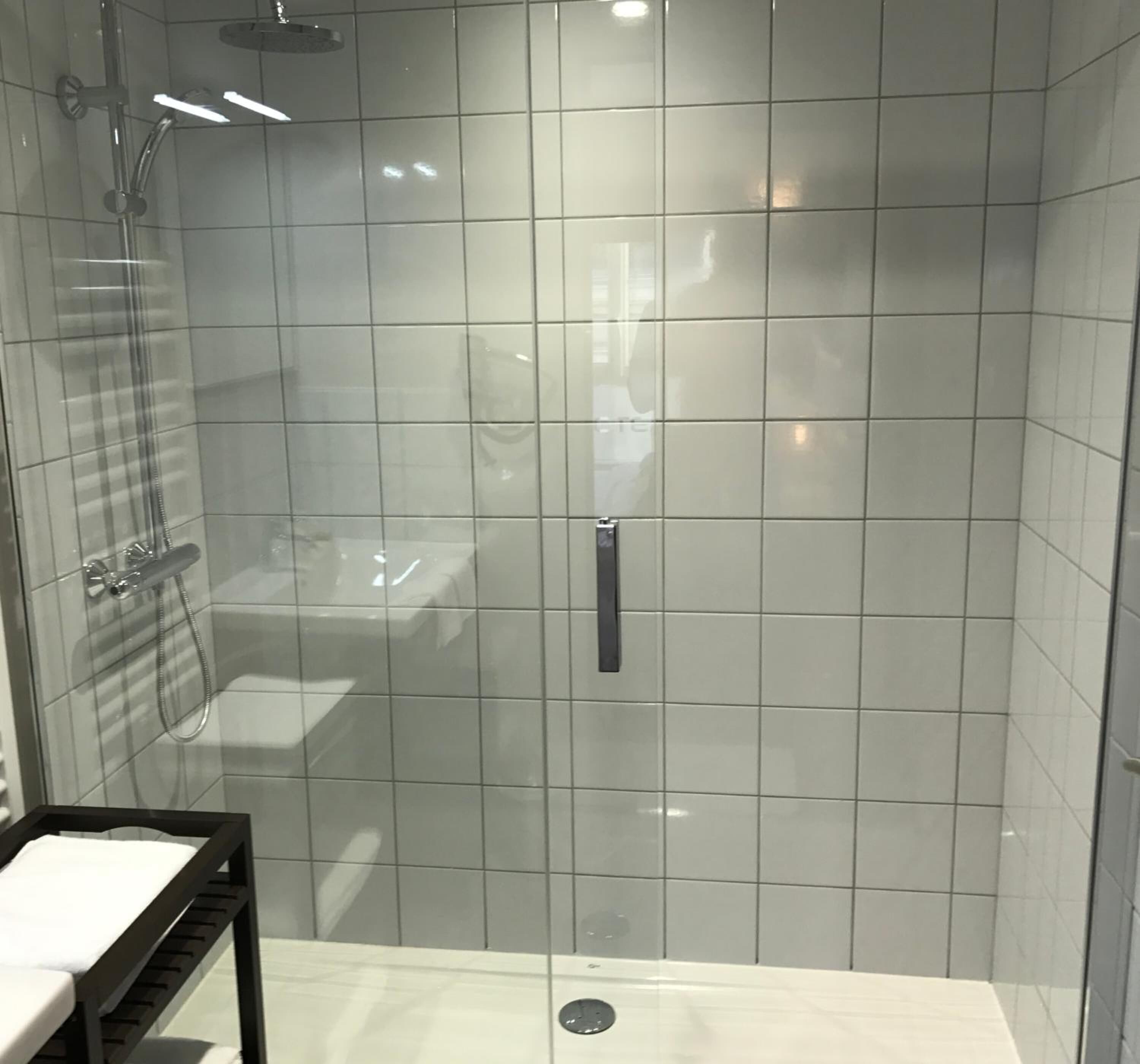 A modern bathroom with a glass-enclosed shower, a white sink, and a black towel rack.