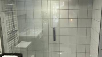 A modern bathroom with a glass-enclosed shower, a white sink, and a black towel rack.