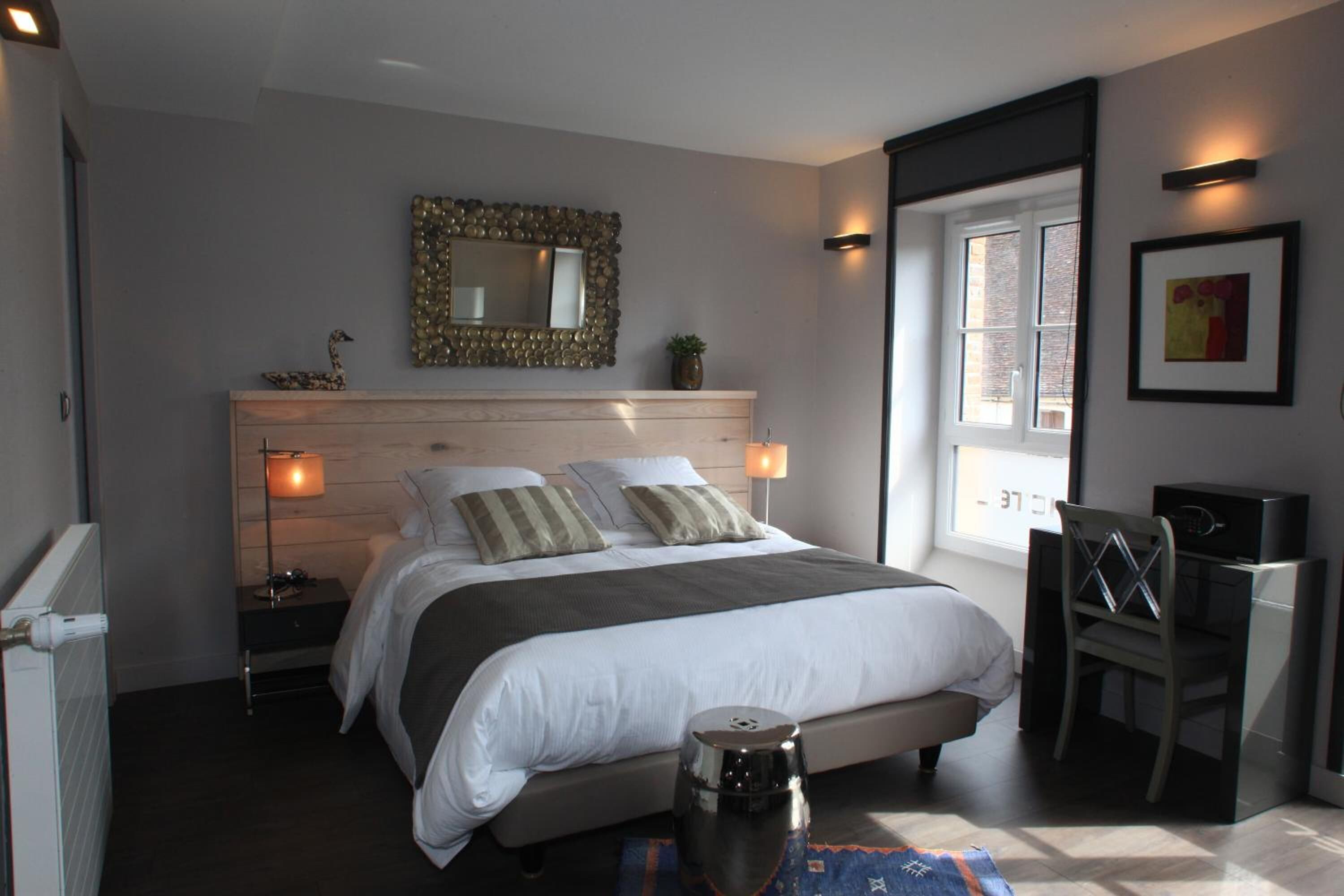 Une chambre à coucher comprenant un lit, des tables de chevet, un miroir, une fenêtre et un bureau avec une chaise.
