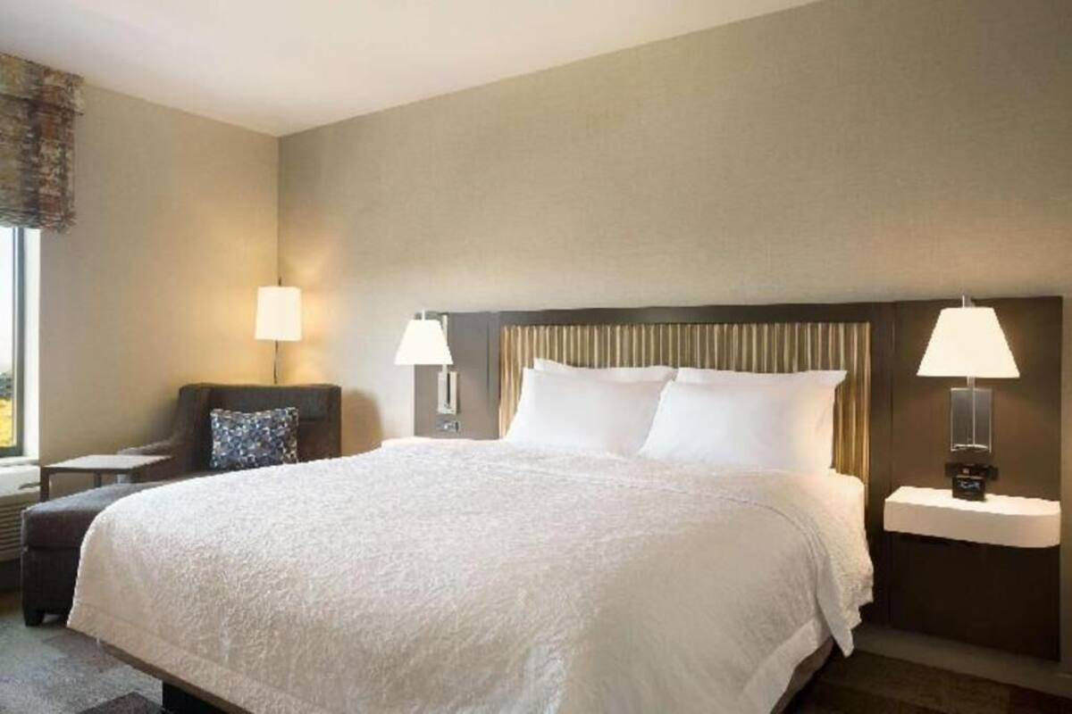 Una habitación de hotel con una cama grande, dos lámparas de noche, una silla y una mesita de noche.