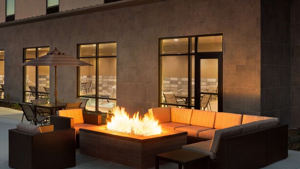 An outdoor seating area with a fire feature, wicker furniture, and large windows. - Hampton Inn Salt Lake City Cottonwood UT (Salt Lake City)