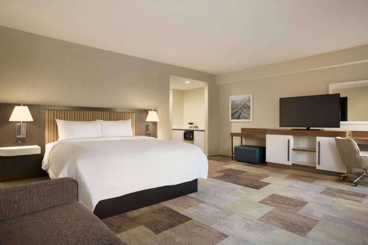 Habitación de hotel con una cama grande, un escritorio, un televisor y una silla.